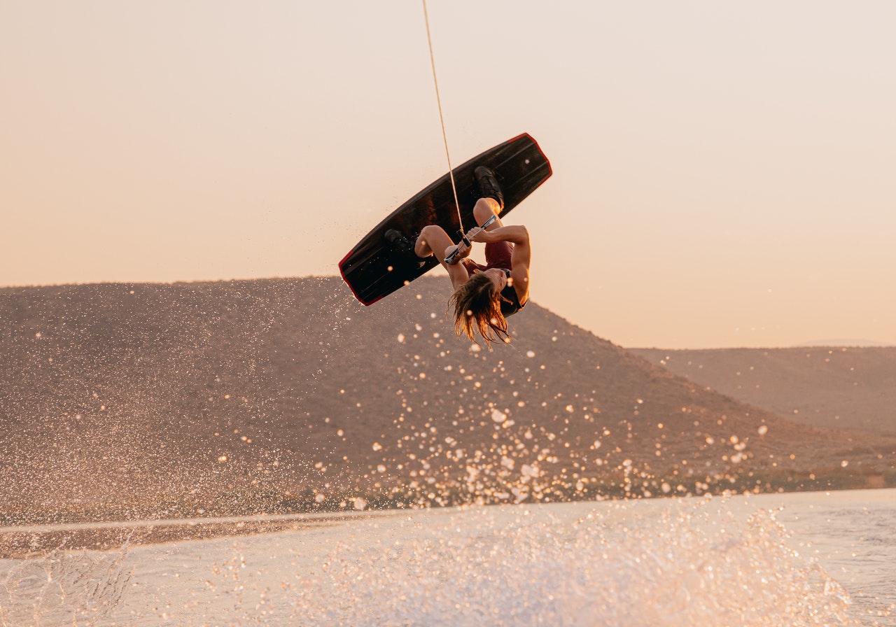 Wakeboarder inverted mid-air with water spray at sunset